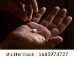 Small photo of A man's hand holding a white pill. Hand holding a red capsule. on black background. Free space to write. Drug for legal use. Pharmacotherapy.