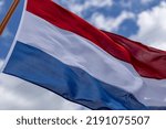 Small photo of Intrinsic folds in tricolor of Dutch national flag blowing in a strong wind with texture and detail against a blue sky with clouds