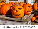 Small photo of Carved halloween pumpkins on the market on sunny day. Pile of orange large Halloween pumpkins used for carving. Many large Halloween 'Ghostride' pumpkins on shelves. Scary Jack O Lantern Halloween