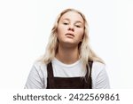 Small photo of A capricious teenage girl. A cute blonde with freckles in a white t-shirt and brown overalls with arrogent face. White background. Close-up.