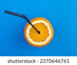 Small photo of Half an orange with tubule for cocktail on the blue background. Top view. Close-up.