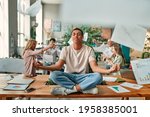Keep calm and no stress! Young African-American man is sitting in lotus position while his colleagues are arguing nearby. Multiracial people working together in modern office.