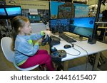 Small photo of Little girl sitting in front of monitors and playing with combat reconnaissance vehicle simulator. Exhibition Arms and Safety. October 12, 2018. Kiev, Ukraine