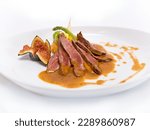 Sliced pan-seared duck breast served with fig sauce, on mashed sweet potatoes, asparagus, and parsnips. Creative cooking. Side view on white background.