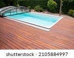 Outdoor swimming pool with cover enclosure and teak wood deck, exotic teakwood flooring stripes around blue water pool