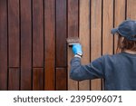 Small photo of Handywoman applying protective varnish or paint with brush on wood fence wall cladding close up. Hardwood cladding house improvement diy concept