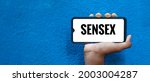 Small photo of SENSEX word on smart phone screen isolated on blue background with copy space for text. Stock Exchange Sensitive Index.