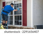 Small photo of A Caucasian man on a ladder wearing blue latex gloves and listening to ear buds washing a window with a squeegee