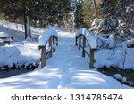 Small photo of This cute wooden bridge is covered in snow and so is the picnic table just across the stream. Unfrozen water still flows beneath. Beautiful evergreens frame the scene. Pretence Park, Ashland, Wis.