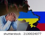 A failed investor sitting sad in front of laptop with Ukraine and Russia flag with stock market chart turn red and going down. Economic crisis because of the war concept.