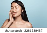 Small photo of Beauty.Woman applying skincare product on her face. Asian girl with smooth perfect skin, touches her skin with pleased smile, enjoys facial cream rejuvenation effect, stands over blue background