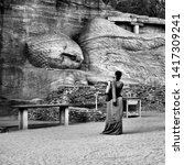 Small photo of AN ENTHUSED VISITOR LOOKS WITH AMAZEMENT AT THE BIG SLEEPING BUDDHA, SRI LANKA - APRIL 02, 2019: A female is spellbound while looking carefully at the huge sleeping Buddha in Polonnaruwa, Sri Lanka.