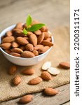 Small photo of Delicious sweet almonds on the wooden table, roasted almond nut for healthy food and snack, Almonds nuts on white bowl and green leaf on sack background