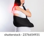 Small photo of A girl on a white background with a black supporting medical bandage after a dislocation of the shoulder joint and a bone fracture. Rehabilitation after injury, orthopedics.