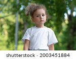 Portrait of beautiful attractive child, little pretty girl kid in white T shirt walking in a park at sunny summer weather, looking at camera with a serious look.