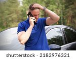 Sad upset guy driver is standing near broken car after road accident, crash, calling emergency on cell mobile phone talking on smartphone. Young desperate man got into accident holding head with hand 