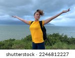 Happy young beautiful carefree woman traveler is hiking, travelling, enjoying freedom, walking on top of mountain with sea, beach view, breathing deep deeply fresh sea, ocean air, rising hands up