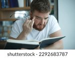 Small photo of tired overworked guy, exhausted young man in glasses college or university student is study hard in library, lesson, problem with eyes, myopic purblind. Vision eyes problems, myopia, blindness.
