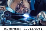 Small photo of Close-up Portrait of Focused Middle Aged Engineer in Glasses Working with High Precision Laser Equipment, Using Lenses and Optics for Accuracy Electronics. Testing Superconductor Material