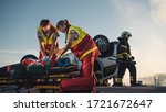 Small photo of On the Car Crash Traffic Accident Scene: Paramedics Saving Life of a Female Victim who is Lying on Stretchers. They Apply Oxygen Mask, Do Cardiopulmonary Resuscitation / CPR and Perform First Aid