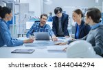 Small photo of Modern Factory Office Meeting Room: Multi Ethnic and Diverse Team of Engineers, Managers and Investors Talking Sitting at Conference Table, Analyzing Blueprints. High-Tech Manufactory Optimization