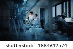Small photo of Modern Medical Research Laboratory: Two Scientists Working, Using Digital Tablet, Analyzing Test, Talking. Advanced Scientific Pharmaceutical Lab for Medicine, Biotechnology Development. Evening Time