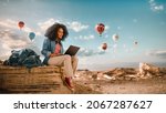 Small photo of Excited Beautiful Young Multiethnic Female Traveller with Afro Hairstyle Using Laptop Computer on Top of Rocky Canyon Valley. Hot Air Balloons Fly in Mountain National Park. Hiking in Nature.