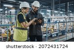 Small photo of Male Specialist and Female Car Factory Engineer in High Visibility Vests Using Tablet Computer. Automotive Industrial Manufacturing Facility Working on Vehicle Production. Diversity on Assembly Plant.