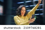 Small photo of Street Shot: Portrait of Beautiful Latin Woman Using Smartphone, Celebrating Successful Victory with Yes Gesture. Smiling Hispanic Female Entrepreneur Using Mobile Phone Happily. Blur Motion Shot.