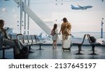 Small photo of Airport Terminal: Beautiful Mother and Cute Little Daughter Wait for their Vacation Flight, Looking out of Window for Arriving and Departing Airplanes. Young Family in Boarding Lounge of Airline Hub