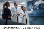 Small photo of Medical Science Hospital Lab Meeting: Diverse Team of Neurologists, Neuroscientists, Neurosurgeon Consult TV Screen Showing MRI Scan with Brain Images, Talk About Treatment Method, New Drugs Cure