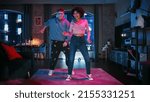 Small photo of Beautiful Stylish Multiethnic Couple in Casual Outfits and Futuristic Neon Glowing Glasses, Dance and Enjoy Life at Home in Loft Apartment. Recording Funny Viral and Active Videos for Social Media.