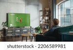 Small photo of Sports Fan Watches Important Soccer Match on TV at Home, He Is Focused on Intense Championship, Cheering for His Team. His Successful Team Scores and Leading the Game.