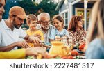 Small photo of Portrait of a Happy Senior Grandfather Holding His Bright Talented Little Grandchildren on Lap at a Outdoors Dinner Party with Food and Drinks. Family Having a Picnic Together with Children.