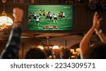 Small photo of Group of American Football Fans Watching a Live Match Broadcast in a Sports Pub on TV. People Cheering, Supporting Their Team. Crowd Goes Ecstatic When Team Scores a Goal and Wins the Championship.