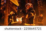 Small photo of Portrait of a Handsome Caucasian Professional Firefighter Methodically Extinguishing a Forest Fire with a Fire Hose. Firemen Brigade Rescuing Wildland from Uncontrollable Arson.
