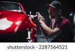 Small photo of Red Sportscar Standing in a Stylish Detailing Dealership Studio. Professional Worker Buffing the Body from Light Scratches, Removing Swirls and Paint Defects from a Fender of the Vehicle