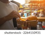 Man hands holding street food burger with french fries on craft paper. Street fast food. festival background