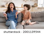 Small photo of Exhausted mummy helpless scream stressed with disobedient preschool son distracting her from surfing web or online shopping in smartphone app. Stubborn misconduct kid annoy desperate tired mom at home