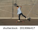 Man riding longboard perform tricks on skateboard in urban street skatepark. Casual hipster guy wearing jeans shirt and bandana skateboarding. Leisure activity, sport extreme, city lifestyle concept