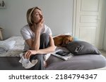 Single depressed mature woman widow loses life sense and motivation. Middle-aged blonde female wearing nightwear sits on bed holding hand on chin looking in distance and waiting for help closeup
