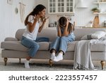 Angry mad mother trying to discipline child, expressing frustration shouting at teenage daughter sitting on sofa covering ears with hands. Psychological effects of yelling at kids, verbal abuse
