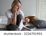 Small photo of Upset middle aged woman with pay bills and calculator sits on bed with dog in home m interior. Perplexed mature female with financial problems stressed when sees too much rent or electricity costs