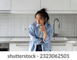 Small photo of Unhealthy Asian woman suffering from strong sudden abdominal throbbing pain, standing in kitchen at home holding glass of water, feeling morning pain, pancreatitis gastritis from unbalanced diet
