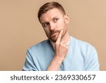 Small photo of Thoughtful puzzled wistful man looking up touching chin by hand on beige background. Pensive guy trying make decision feeling frustration, uncertainty. Life problems, troubles, body language concept.
