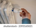Small photo of Hand adjusting heater knob, regulating temperature at home in winter during heating season. Radiator equipped with thermostat allowing to save, economize energy, limit temperature in apartment