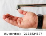 A faucet with water drops and a hand on a blurred background of a light curtain in the bathroom. The concept of lack of water. Disconnection and violation of water supply. Background with copy space