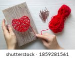 Step by step instruction: DIY gift for Valentine's Day. step 3: hands are tying red threads on nails in the heart-shaped painting. red threads and nails are lying nearby