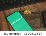 Small photo of Robinhood app green logo with gold Bitcoin in a brown waller and keyboard on wood backround. WARSAW, POLAND - FEBRUARY 17, 2021