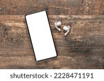 modern smartphone with blank white screen for inserting an inscription or logo with wireless earphones on wooden background. Audio technology apps, music podcasts books